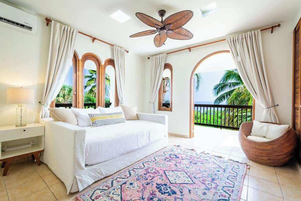 Bedroom with white linens, daybed and ocean view through arched windows
